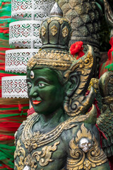 Close-up of an ornate green deity statue with gold adornments and crown. This majestic guardian is from the Mahadevalai Ganesha complex in Bangkok, Thailand.