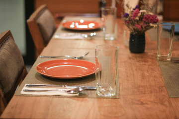 Elegant dining table setting at restaurant awaits guests. empty wooden table features an orange plate, cutlery, and glass, ready for warm and inviting meal