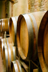 Row of traditional oak barrels in a rustic wine cellar, used for aging fine wine in a European vineyard, showcasing artisanal winemaking techniques