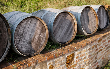Aged wooden barrels outdoors on a rustic brick wall in a countryside vineyard, used for traditional wine fermentation and aging under natural sunlight