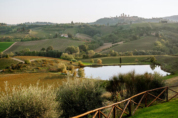 Scenic view of autumn vineyard rows with a reflective pond and rolling hills in the background, Tuscany countryside landscape