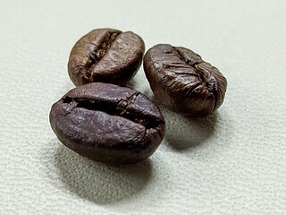 Close-up shot of three roasted coffee beans with detailed textures on a plain backdrop