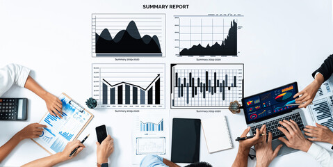 A business team collaborating in a modern office setting, analyzing a summary report with various charts and graphs displayed on a table filled with devices. Axiom