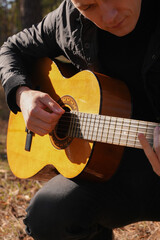 Beautiful blonde man playing acoustic guitar and singing relaxing enjoying outdoors on sunny autumn day. Artist learning and practicing playing musical instrument. Fall leaves autumnal weather 