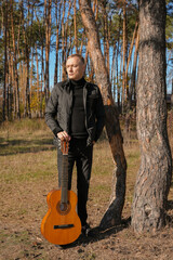 Portrait of smiling caucasian artist plays wooden acoustic guitar in autumnal park. Young songwriter plays string musical instrument hobby outside in nature fall time. Audio music healing in natural