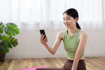 Smiling Japanese Woman in Activewear Using Smartphone at Home