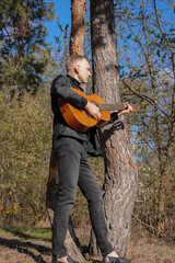 Blonde man playing string guitar outdoors in autumn forest. Concept of sound therapy, mental health and wellness rituals. Calmness tranquility audio-sensory practices. Aura farming energy holistic