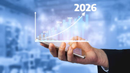 A close-up of a hand holding a smartphone with a financial growth chart emphasizing future projections from 2023 to 2026 in a modern office setting. Tessel