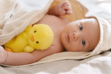 Happy curious baby child after bath with towel on head. Adorable little boy wrapped in blanket. Cutest 3 months old baby smiling in towel on bed close up at home. Child caring routine.