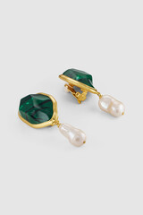 Emerald green stone and pearl drop earrings on a plain background