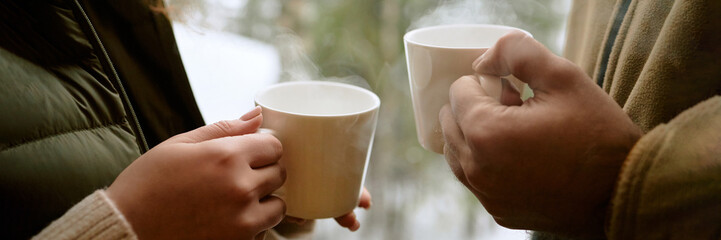 Header of woman and man holding mugs with both hands, standing close together, steam rising from...
