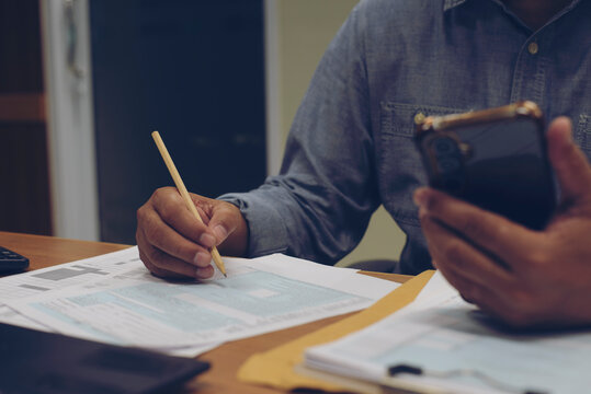 Season to pay Tax and Budget planning concept. Businessman calculating annual tax and using mobile phone. calculator, personal income tax form, laptop, report placed on home office desk.