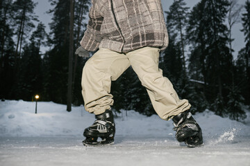 Child ice skating outdoors on frozen surface in winter forest, wearing skates and moving forward with bent knees, snow and trees visible in background