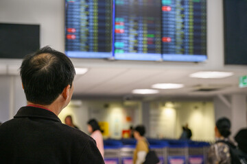 Man looking at the flight information display board at the airport. Unrecognizable passengers in the queue.