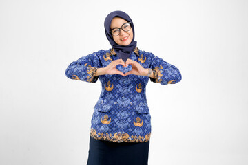 Beautiful teacher wearing batik Korpri uniform making heart hand gesture while smiling warmly....