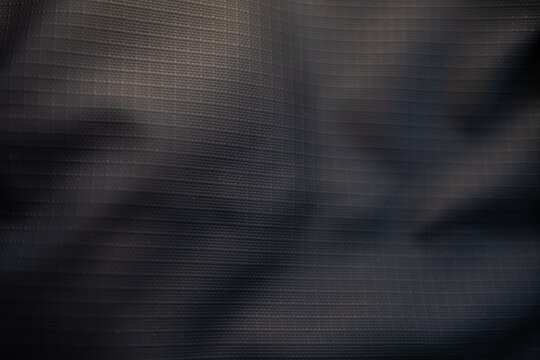 Dark grey ripstop fabric texture. Macro shot of a crumpled, durable synthetic material with a grid pattern, creating an abstract and technical background.
