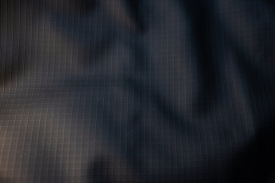 Dark grey ripstop fabric texture. Macro shot of a crumpled, durable synthetic material with a grid pattern, creating an abstract and technical background.