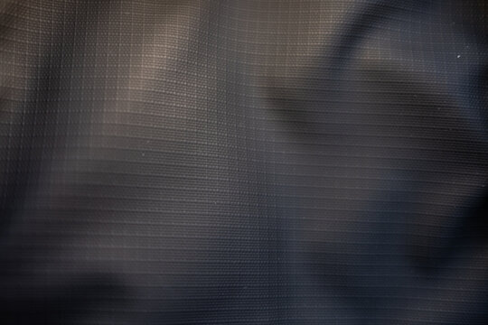 Dark grey ripstop fabric texture. Macro shot of a crumpled, durable synthetic material with a grid pattern, creating an abstract and technical background.