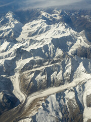 Flying over the European Alps during fall season. Aerial view from the airplane window. Fresh snow on the peaks