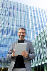 Low angle view vertical portrait of happy mature businessman using digital tablet outdoors in front...