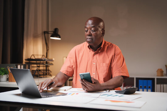 Mature man working on laptop and smartphone at night - Powered by Adobe