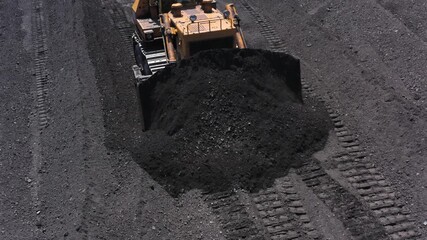 Aerial view of bulldozers transporting coal to conveyor belts at a thermal power plant during daytime operations
