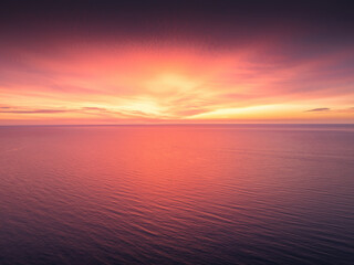 Vibrant Stunning Sea Sunset Sunrise Over Calm Ocean water At Dusk With Reflective Ripple surface of Red And Orange Waves, Aerial view