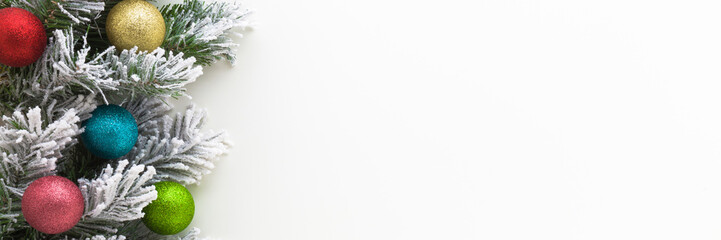 Colorful baubles with glitter, green artificial fir branches covered with hoarfrost and white snow. Light gray table background. Wide banner. Christmas decoration. Empty place for text. Top down view.