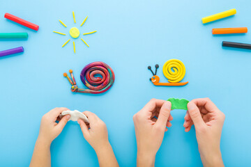 Young adult mother and little child hands making and creating snails from colorful modeling clay on light blue table background. Pastel color. Closeup. Flat lay. Point of view shot. Top down view.
