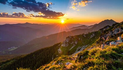 A scenic sunset shines over distant mountains, casting a warm glow on the lush foreground slope and valley below