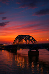 Fototapeta premium Steel arch bridge over river at sunset twilight with city skyline in the background 