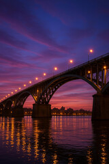 Naklejka premium Steel arch bridge over river at sunset twilight with city skyline in the background 