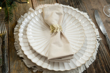 Elegant Christmas table setting with white plates, beige napkin, and decorative napkin ring. 