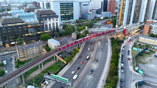Cinematic drone shot of a red train gliding through modern urban towers at sunset, with soft golden light reflecting over city architecture and streets.	
