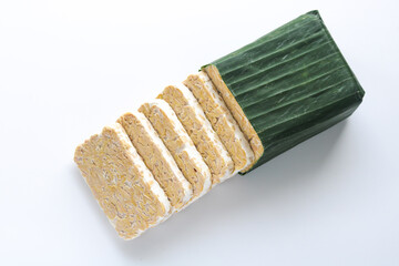 Indonesian tempeh (tempe) wrapped in banana leaf and sliced into thick cuts. A traditional plant-based protein made from fermented soybeans.