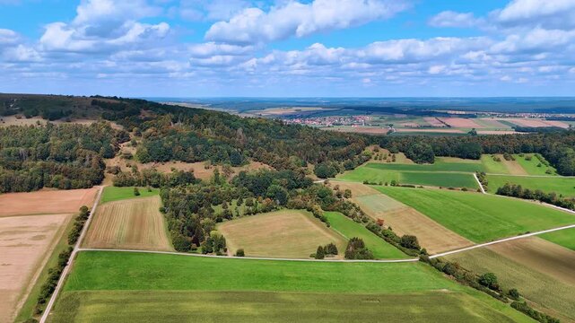 Aerial view of green farmlands and distant hills. Drone view of lush green farmlands and rolling hills with blue sky and scattered clouds.