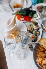 A festive banquet table setting with various appetizers, salads, glasses, and a place card with a handwritten name in Cyrillic