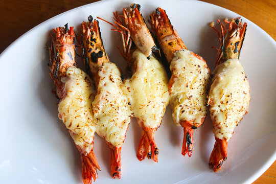 A dish of five large grilled prawns topped with melted cheese, arranged on a clean white plate.