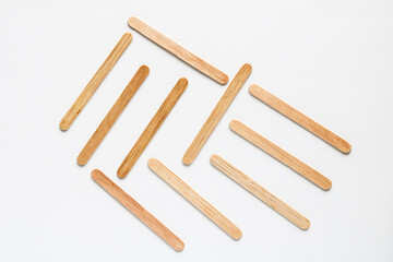 Multiple natural wooden craft sticks or popsicle sticks scattered loosely, creating a dynamic diagonal pattern on a white background.