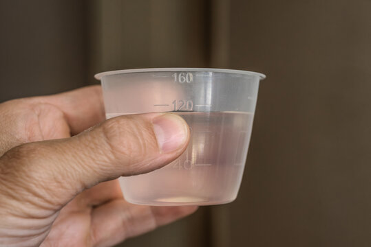 Closeup photo of male hands holding plastic measuring cup with liquid. Hand holding a transparent measuring cup with water for home or medical use.