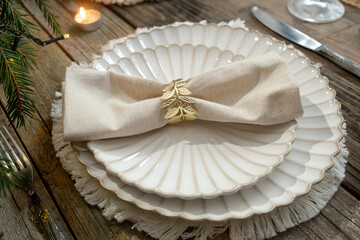 Elegant Christmas table setting. Festive table with white plates decorated napkin and golden ring.