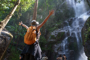 Traveler with orange backpack enjoying waterfall in lush tropical forest