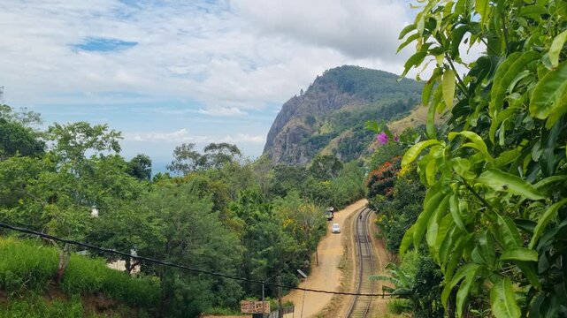 Panoramic view of Ella Rock in Sri Lanka, with the legendary Badulla&ndash;Colombo railway weaving through lush tropical vegetation under a partly cloudy sky
