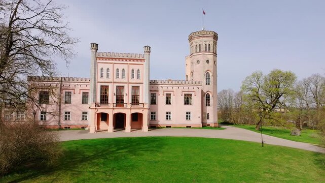 Cinematic spring drone shot showing pink Vecauce Palace with Latvian flag waving