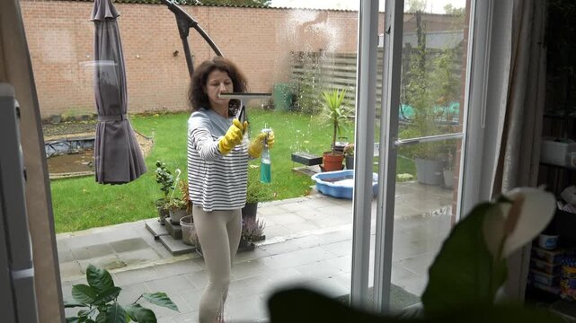 Woman cleaning glass door in backyard on a cloudy afternoon
