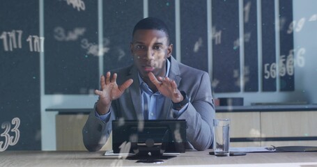 Gesturing businessman in suit explaining data in meeting room with tablet on stand and water