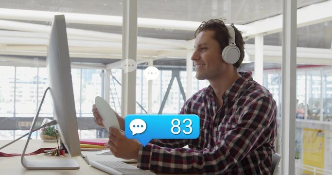 Smiling man in plaid shirt, headphones holding coffee mug, viewing monitor in office with succulent - Powered by Adobe
