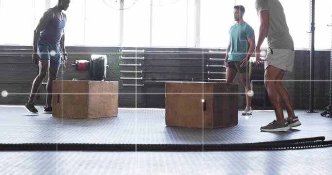 Three men in sportswear performing box jumps in CrossFit gym, with plyometric boxes, battle ropes - Powered by Adobe