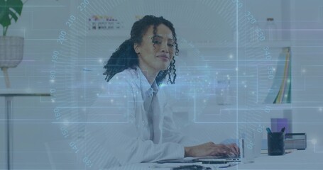 Typing research scientist wearing lab coat over business attire at office desk, with laptop and mug