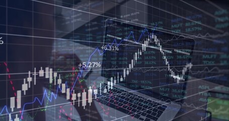 Displaying laptop showing trading charts with percentages on office desk, with smartphone nearby